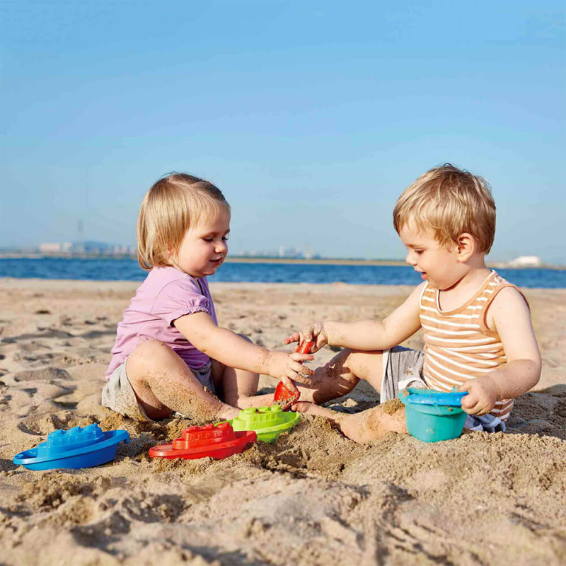 Jeunes enfants dans le sable avec les 3 bateaux en jouet.