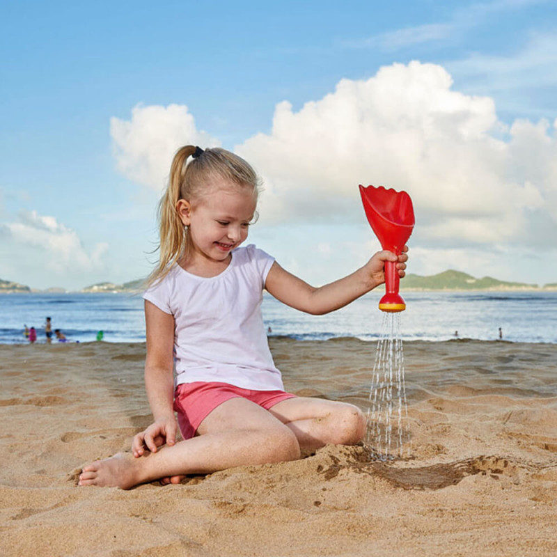 Petite fille avec la pelle à pluie rouge à la plage.