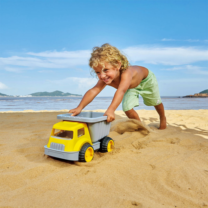 Enfant qui s'amuse à la plage avec un camion benne Hape